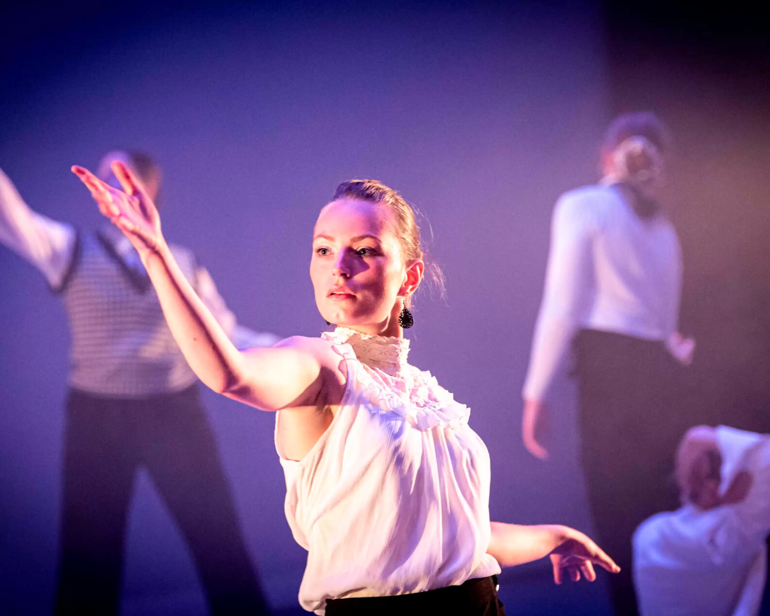 Expressieve jonge danseres op podium met sfeervolle belichting.