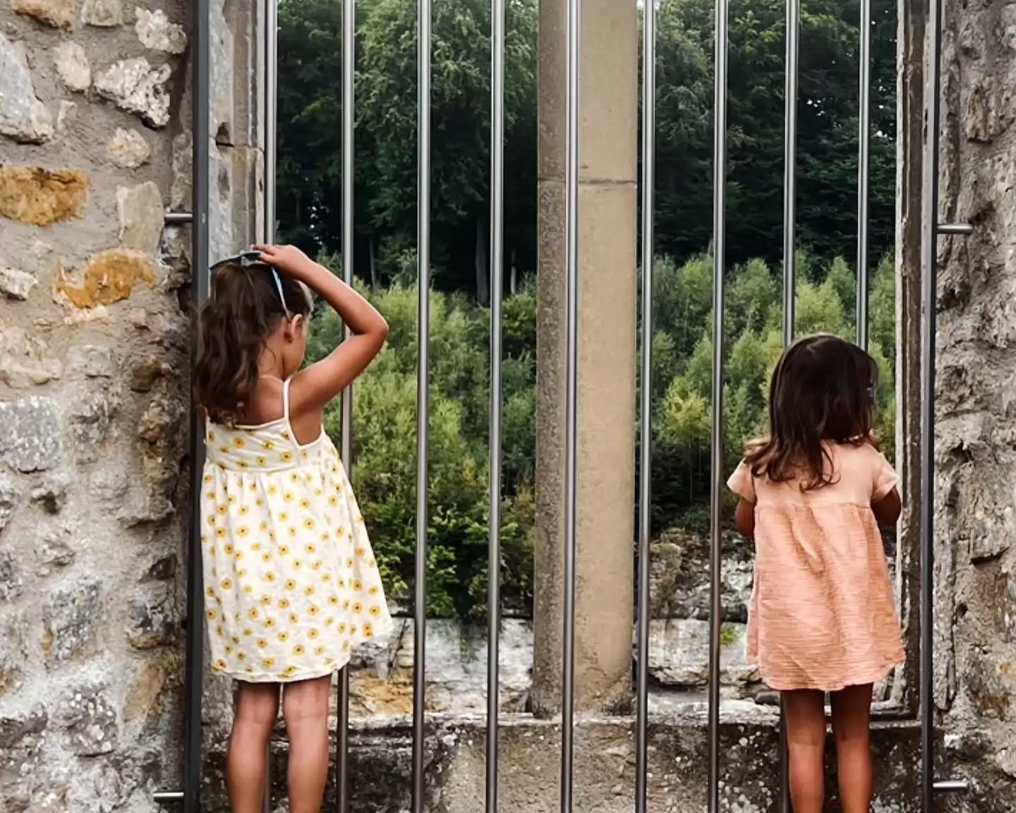 Foto Ine van de Donk: 2 meisjes achter een hek met een waanzinnige wereld voor ze. Symboliek van onderdrukking en er niet automatisch bij kunnen.