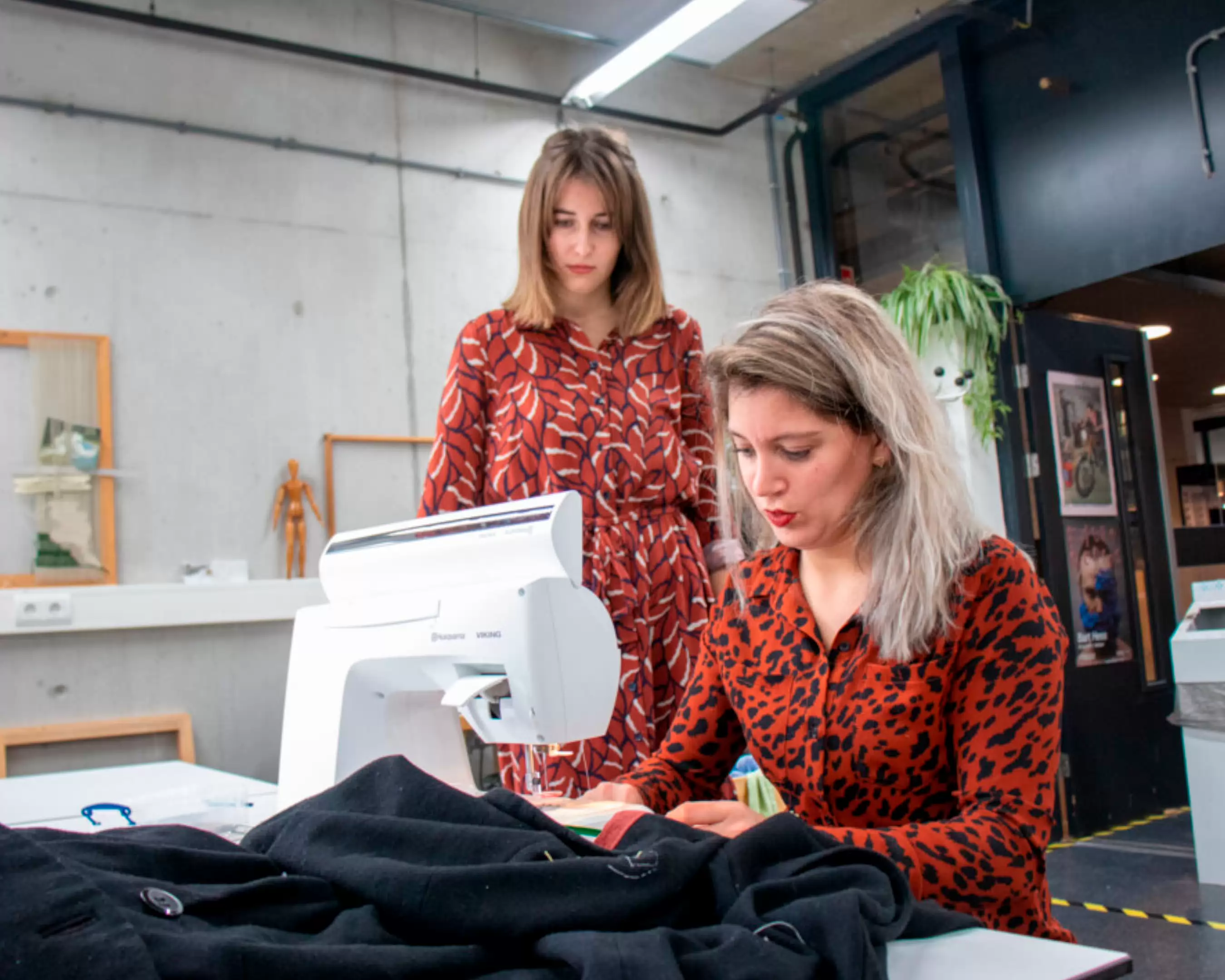 Twee studenten werken aan kleding bij een naaimachine in de werkplaats.