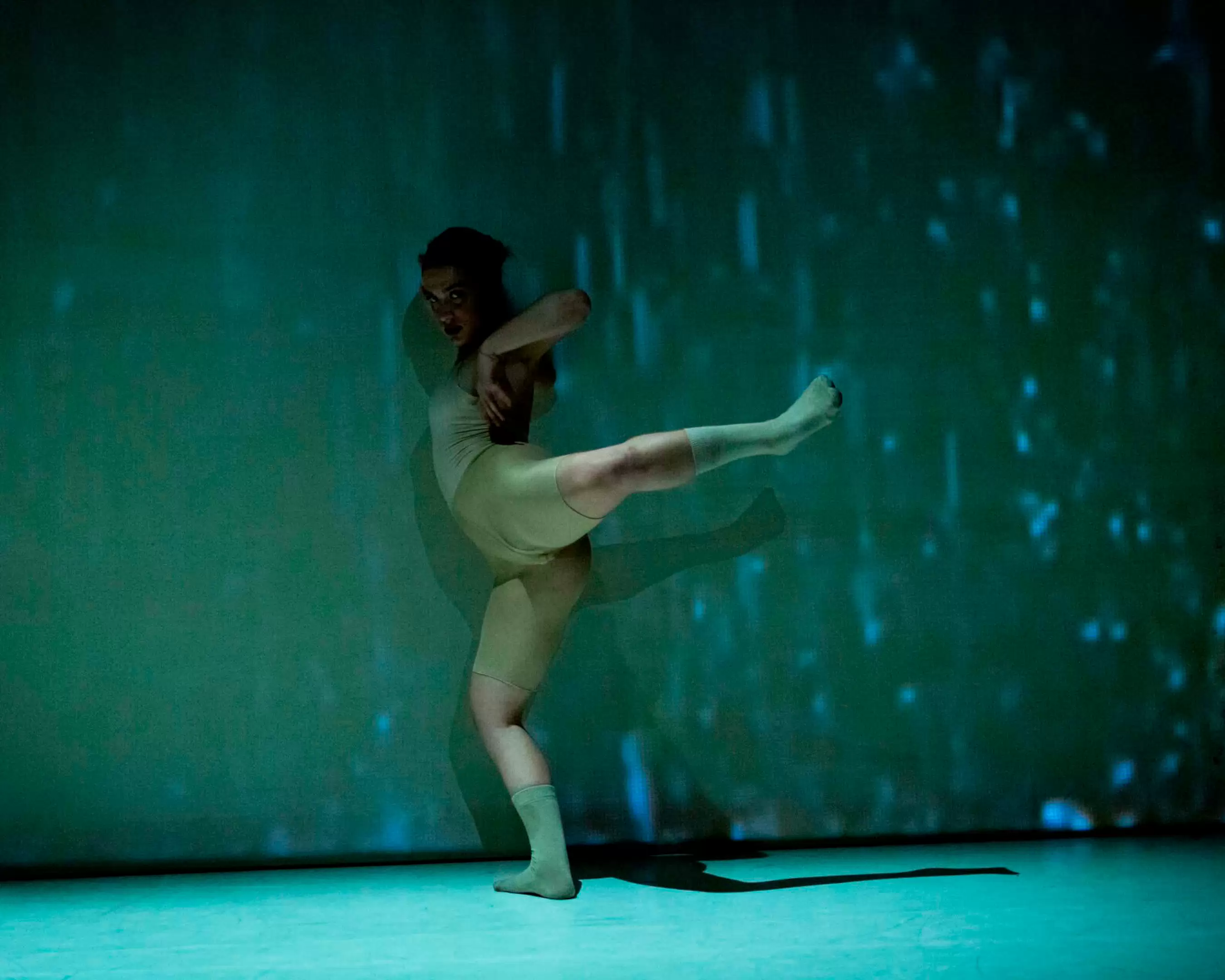 A student from the master Choreography is performing a dance solo. The light is green and blue. She is wearing a tight outfit in skin colour