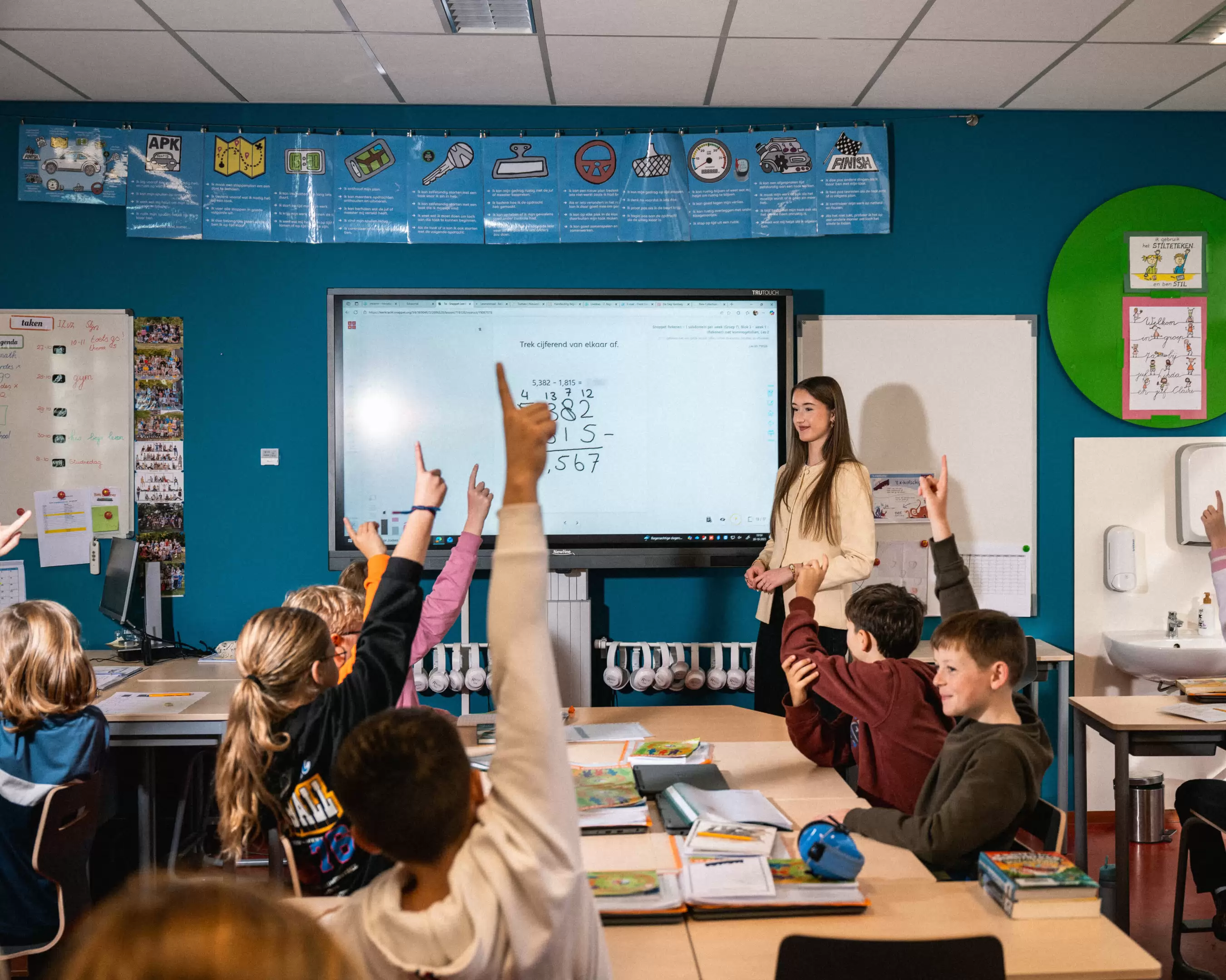 Student voor het digibord, met leerlingen die hun vinger opsteken