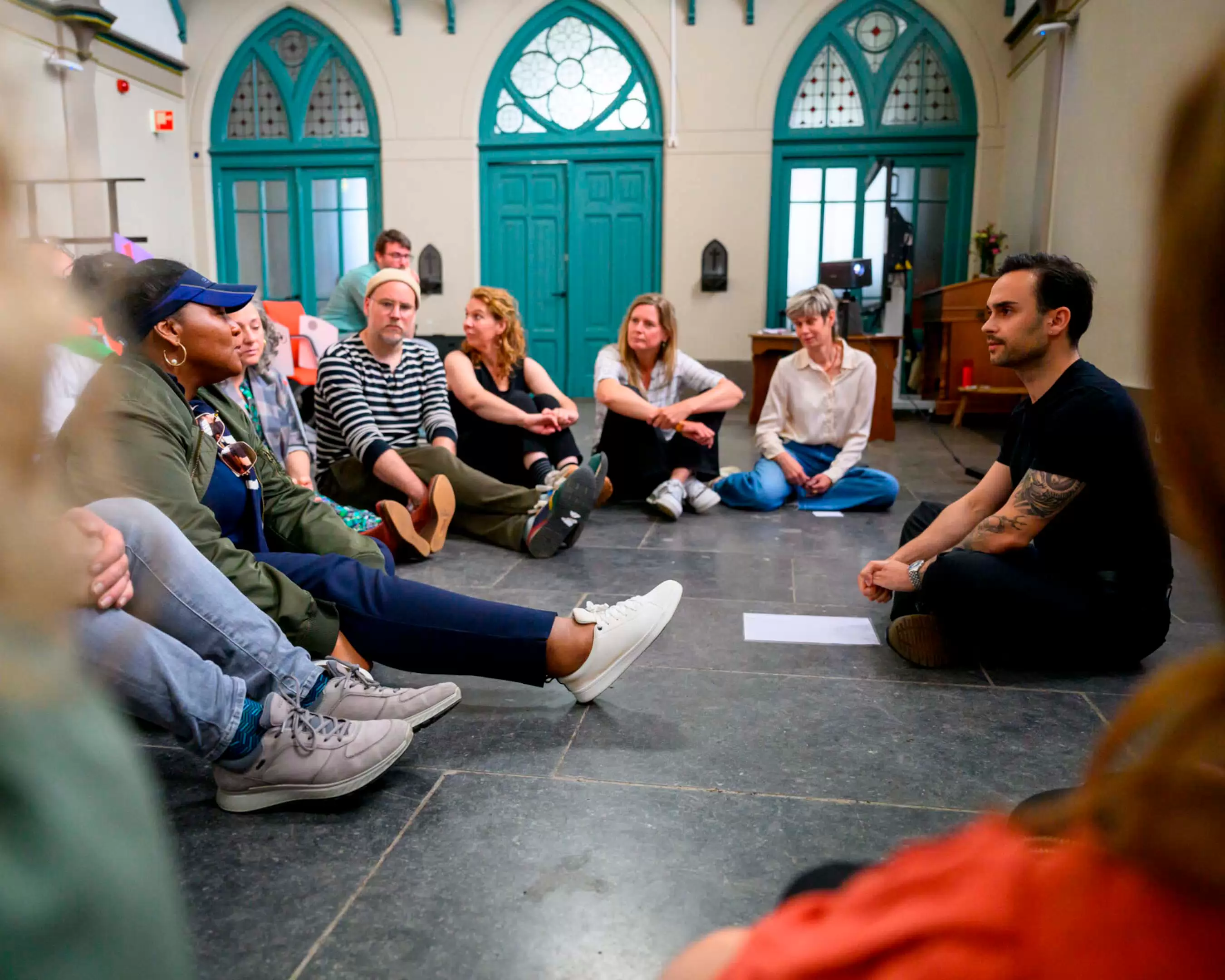 Studenten van de master Kunsteducatie zitten in een kring op de grond van onze kapel. Ze werven gezamenlijk aan een project en zijn in overleg
