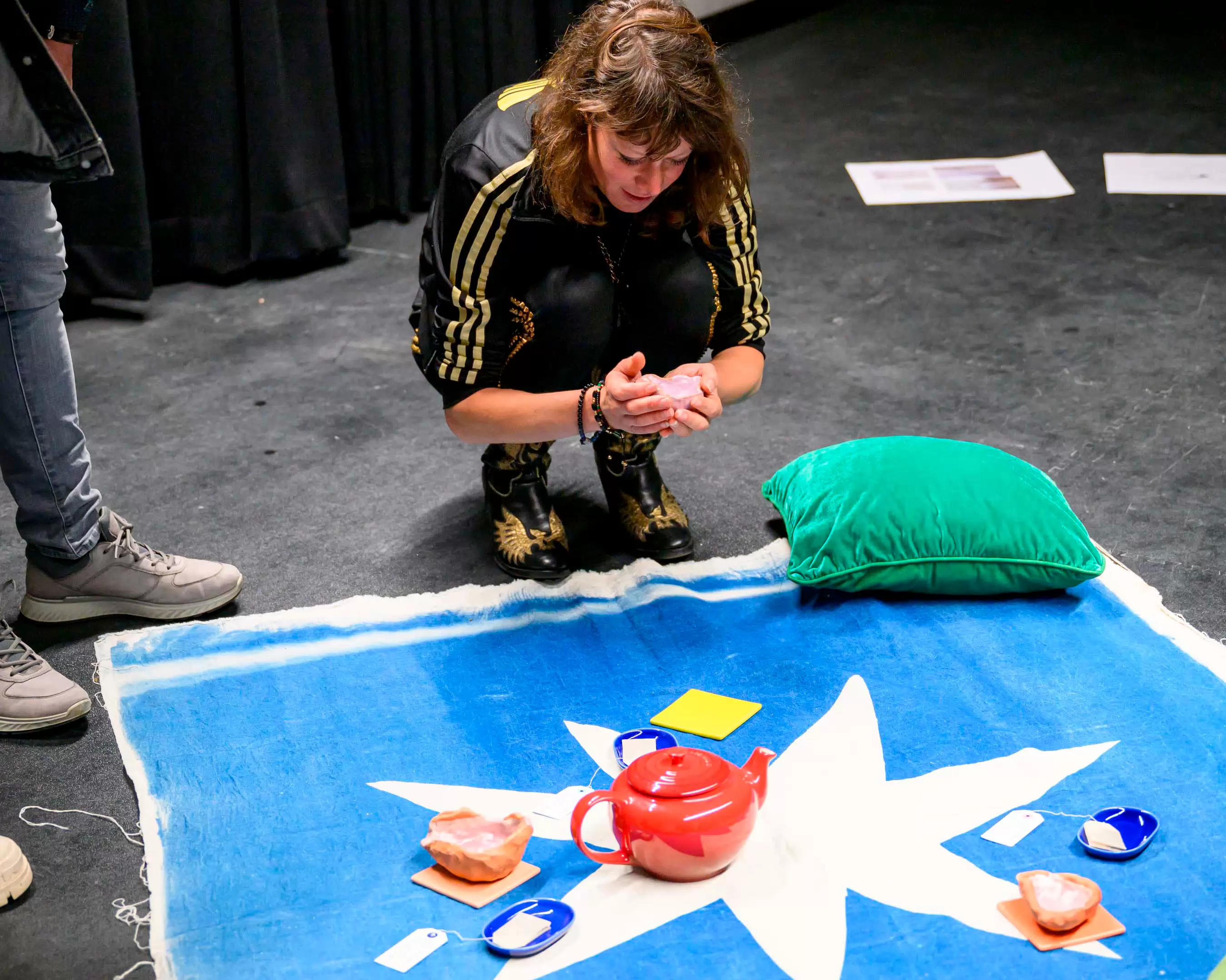 Een student van de master Kunsteducatie werk aan haar project in het theater. Er ligt een blauwe kleed op de grond met een rode theepot erop.