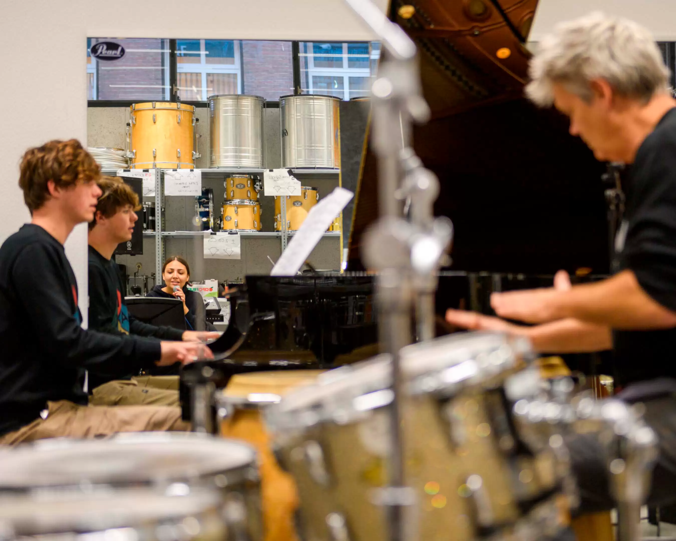 Students are rehearsing on the piano and singing with a teacher
