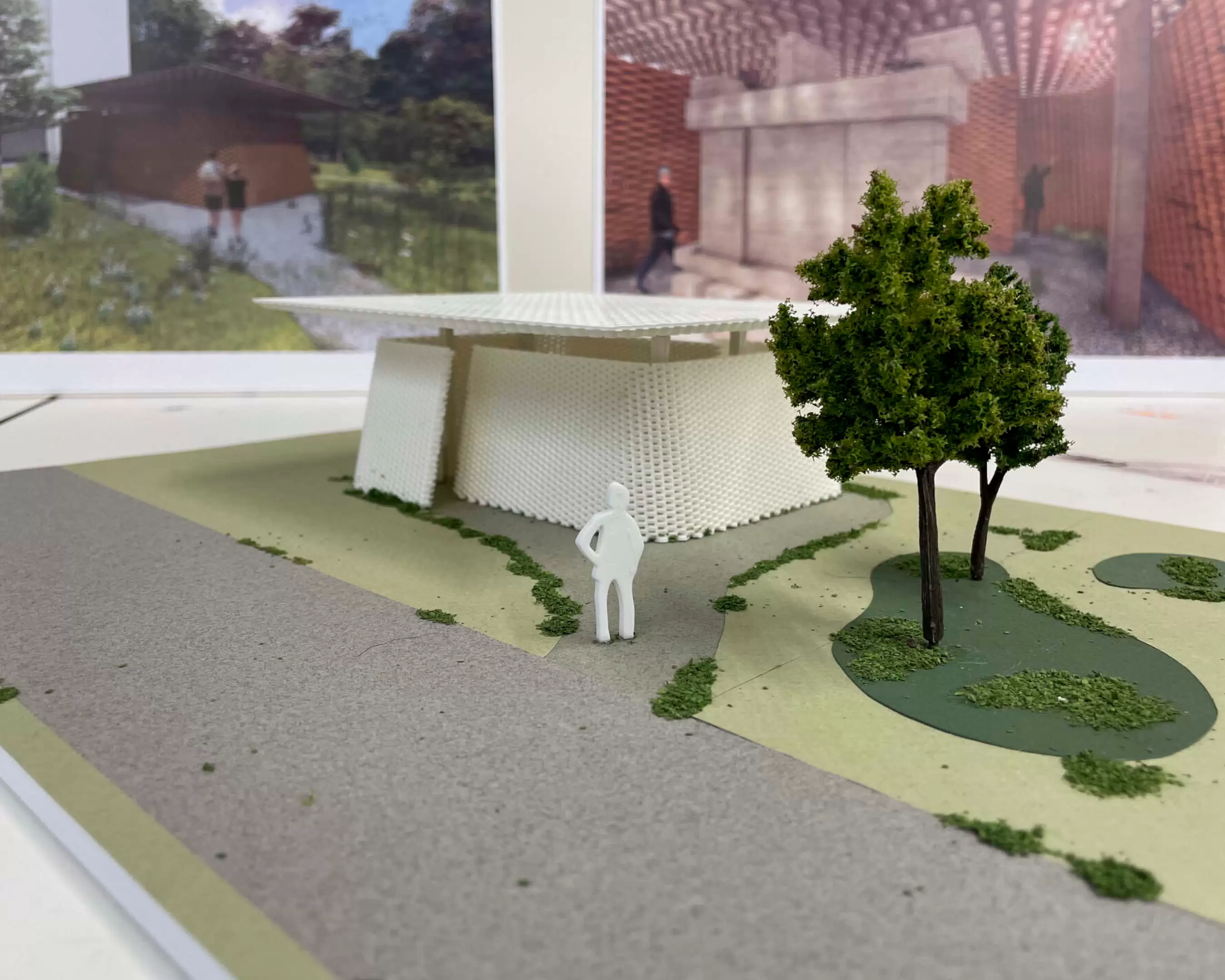 A detailed architectural model created by a student from the Master's program in Urbanism. The model represents a green landscape with trees, grass, and pathways leading to a grey building with arched windows. Small white figurines and structures are placed to add scale and context, depicting a tranquil outdoor environment.