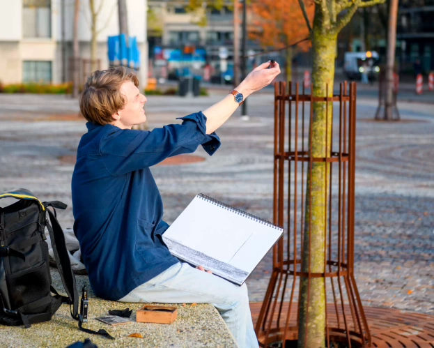 A male student is working on his project outside at a tree