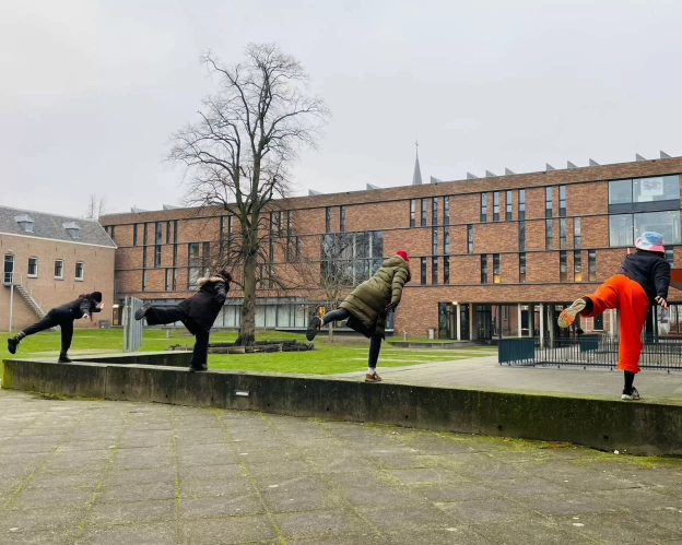 Four students stand with their backs to the camera on 1 leg on the Zwijsenplein campus of Fontys Academy of the Ars.