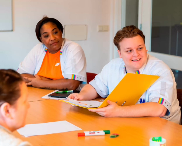Studenten van de opleiding Verpleegkunde in een werksituatie aan een tafel met een dossier.