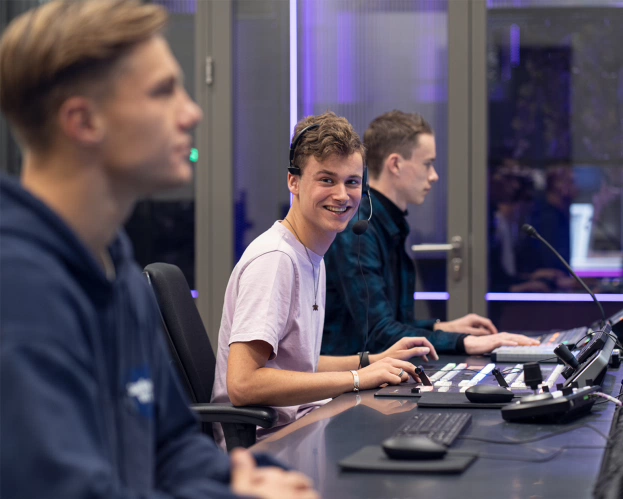 Een backstage moment bij Fontys Journalistiek: drie jongens aan het werk in een van de studio's. De middelste kijkt vrolijk in de camera.