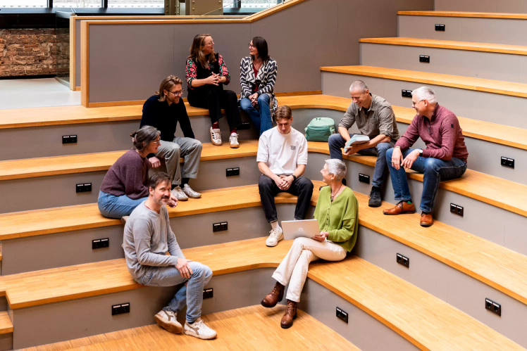 Drie studenten Theologie aan een tafel pratend en lezend