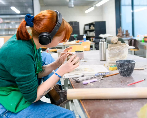 Student werkt geconcentreerd aan een kleiwerkstuk in een atelier.